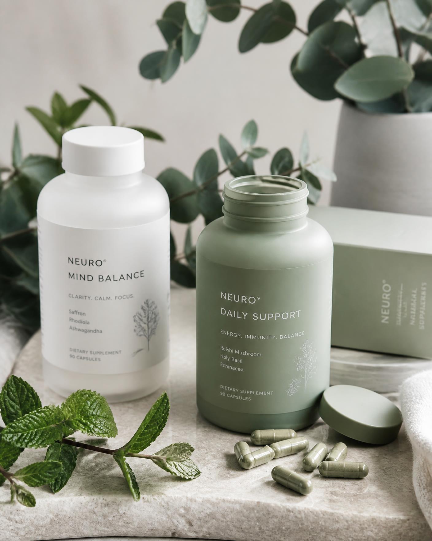 Sage-green supplement bottles, capsules and fresh botanical leaves on pale stone